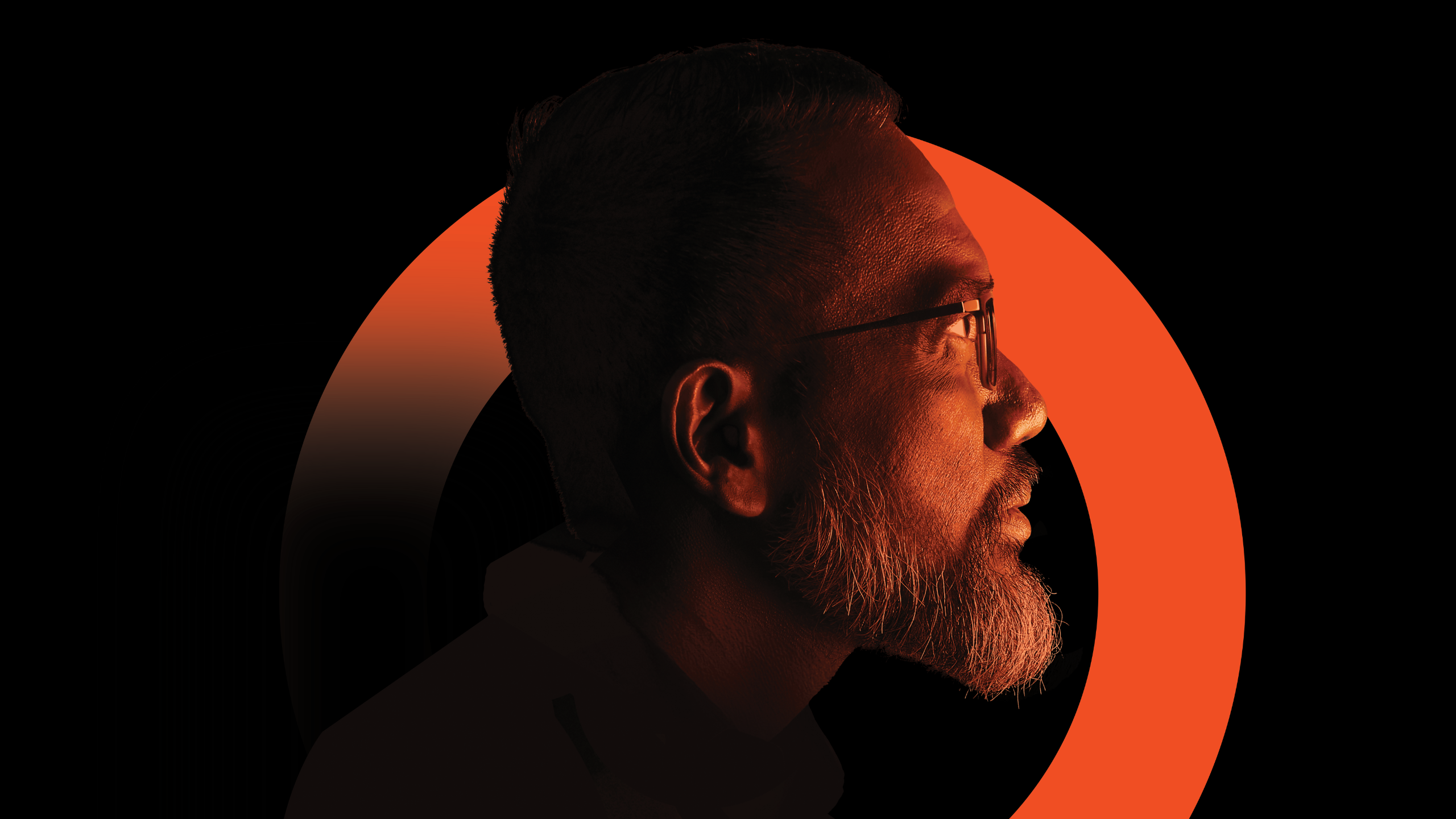 A side profile of a bearded person wearing glasses against a black background with a bold orange circular arc behind them.