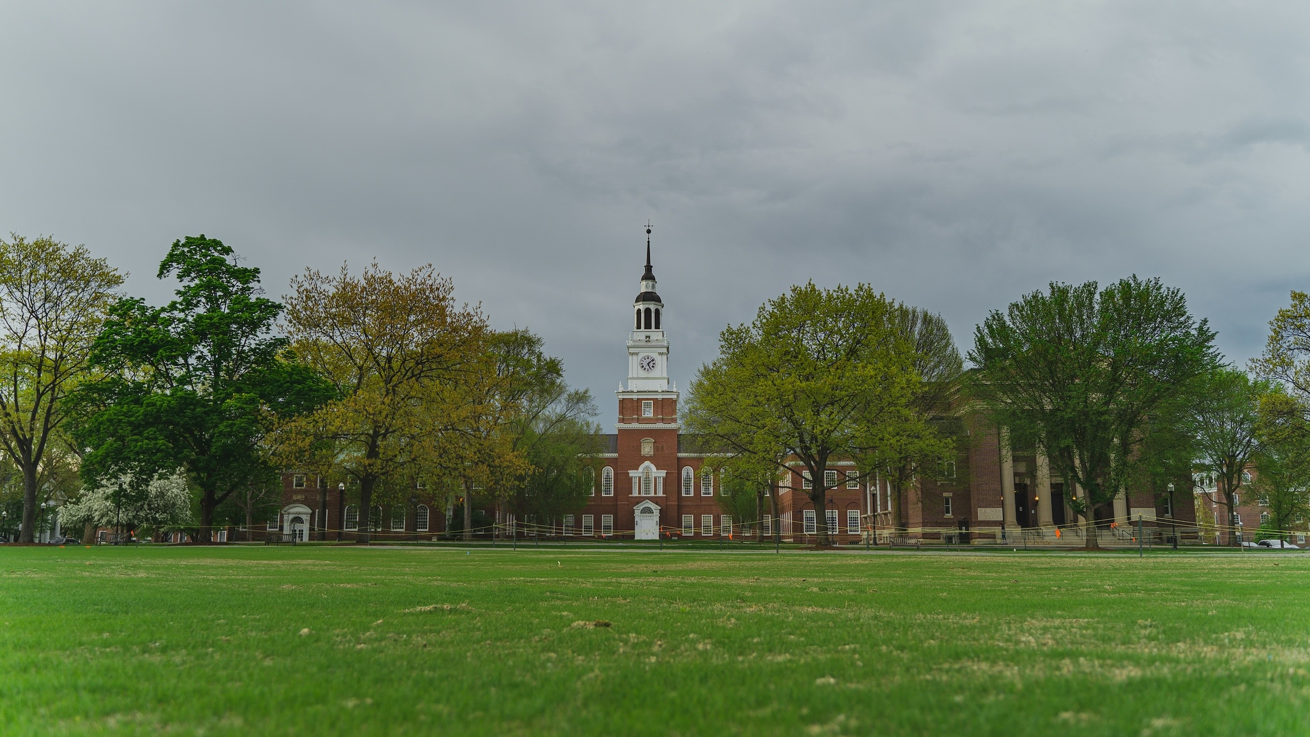 Dartmouth College’s Baker-Berry Library with its iconic bell tower, framed by a green lawn and trees under a cloudy sky.