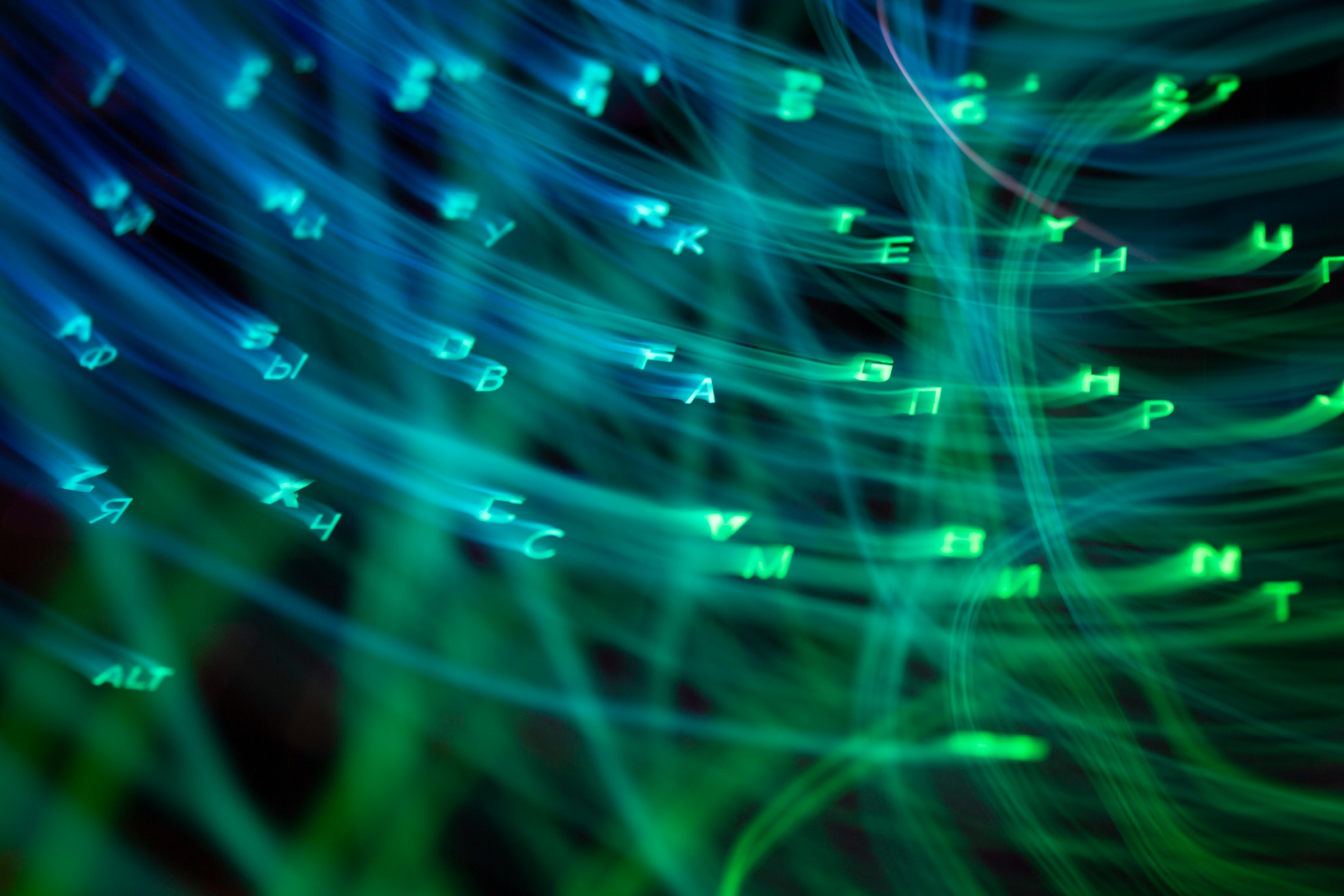 Close-up of a computer keyboard with blue and green backlighting, photographed at an angle with shallow depth of field.
