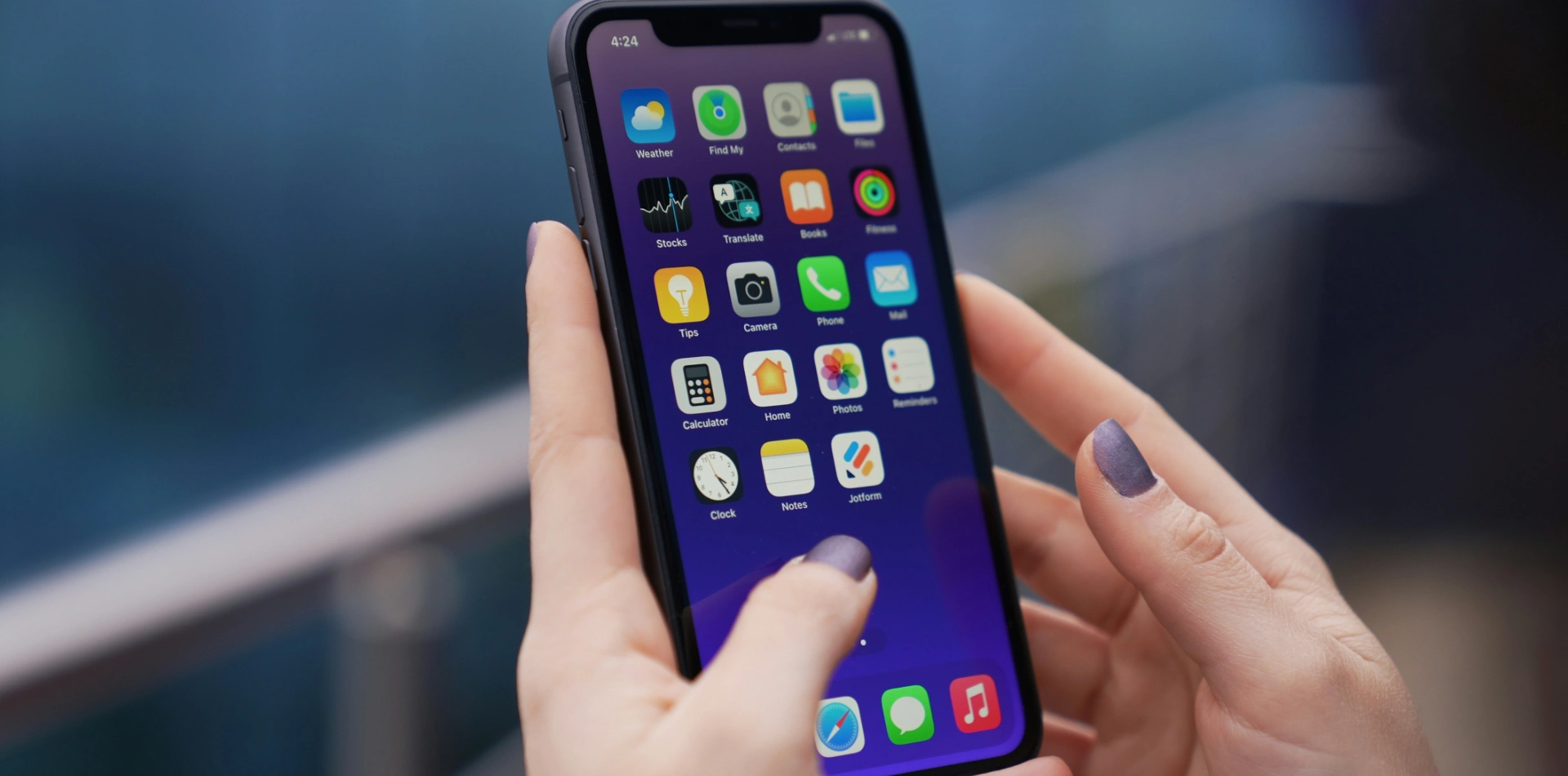 Hands holding an iPhone home screen showing apps including Camera, Phone, Mail, Photos and Notes.
