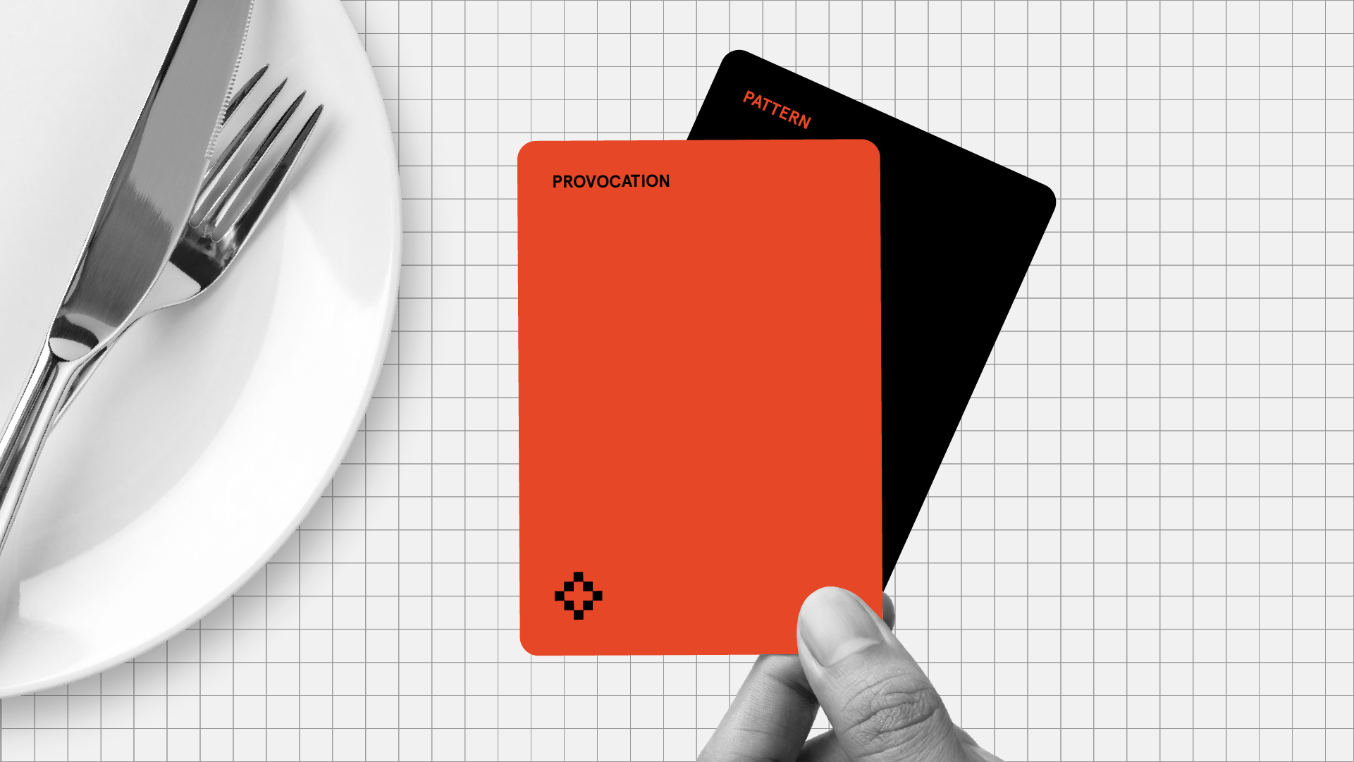 Place setting with white plate, fork, and knife on white grid background. Red card labelled "PROVOCATION" with small black diamond symbol is held in foreground, with black card labelled "PATTERN" visible behind it.