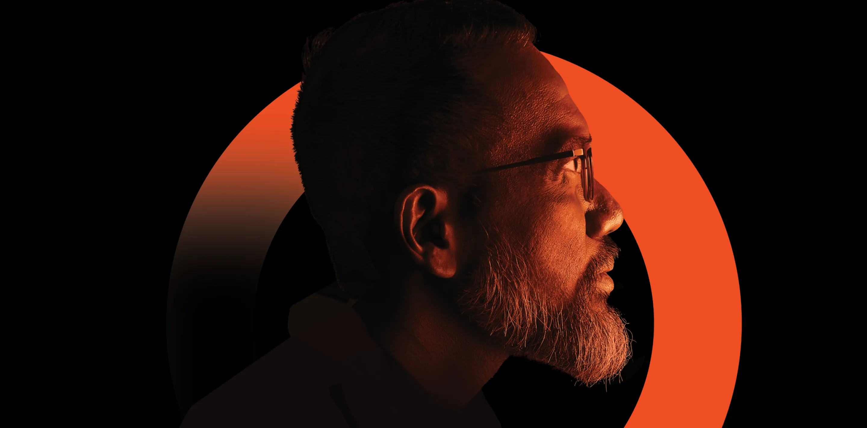 A side profile of a bearded person wearing glasses against a black background with a bold orange circular arc behind them.