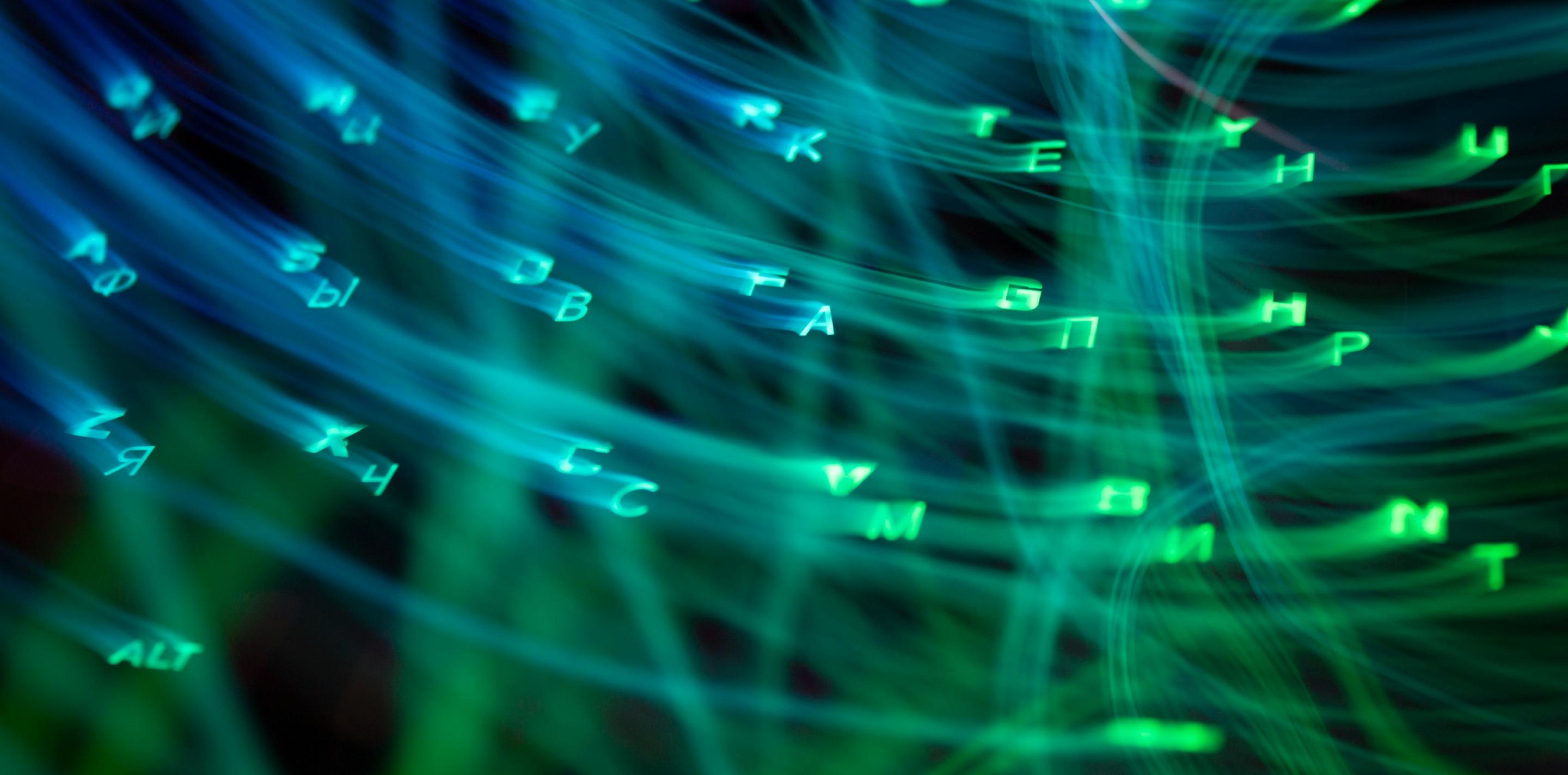 Close-up of a computer keyboard with blue and green backlighting, photographed at an angle with shallow depth of field.