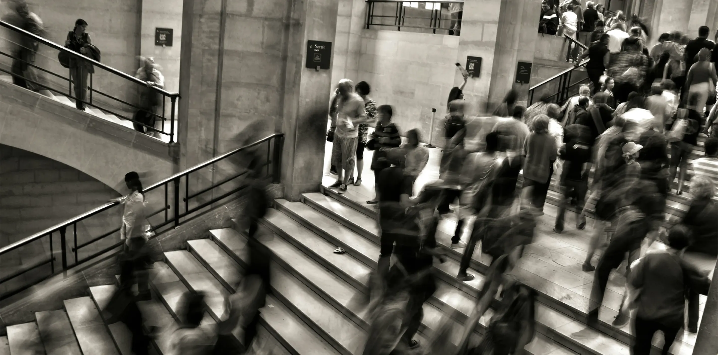 Sepia photo of people walking up and down stairs in an office building.
