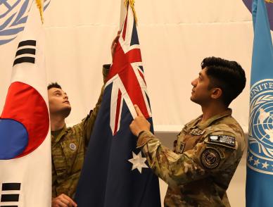 Two soldiers in camouflage positioning the Australian flag between South Korean and United Nations flags.