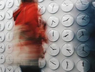 Person in red walking past a wall of white clocks, their figure blurred by motion while the clocks stay sharp.